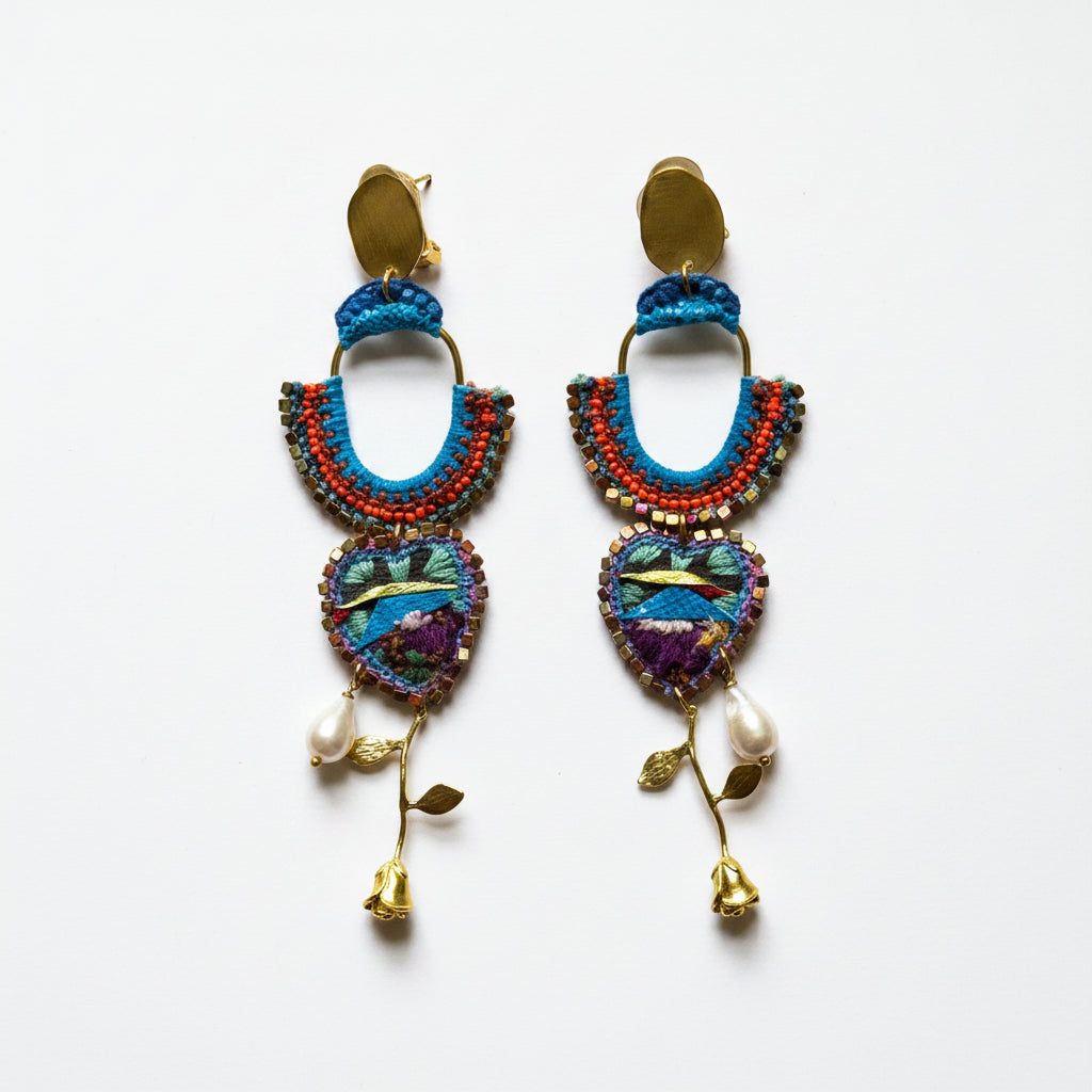 Colorful beaded earrings with heart designs and pearl-like beads on a textured fabric background