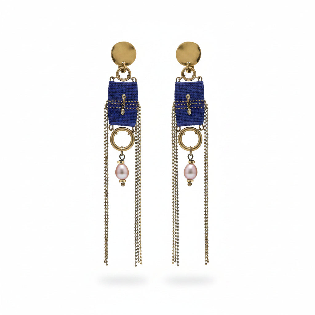 Pair of earrings with blue fabric, chains, and pearls on a textured gray background