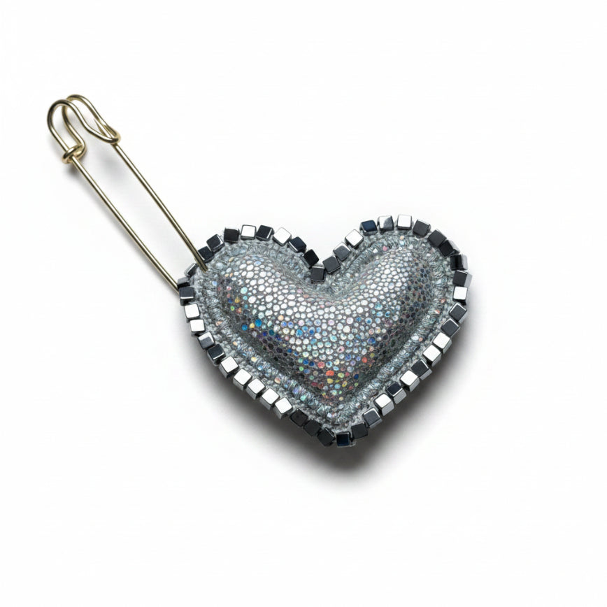 Heart-shaped brooch with metallic beads on a textured gray background