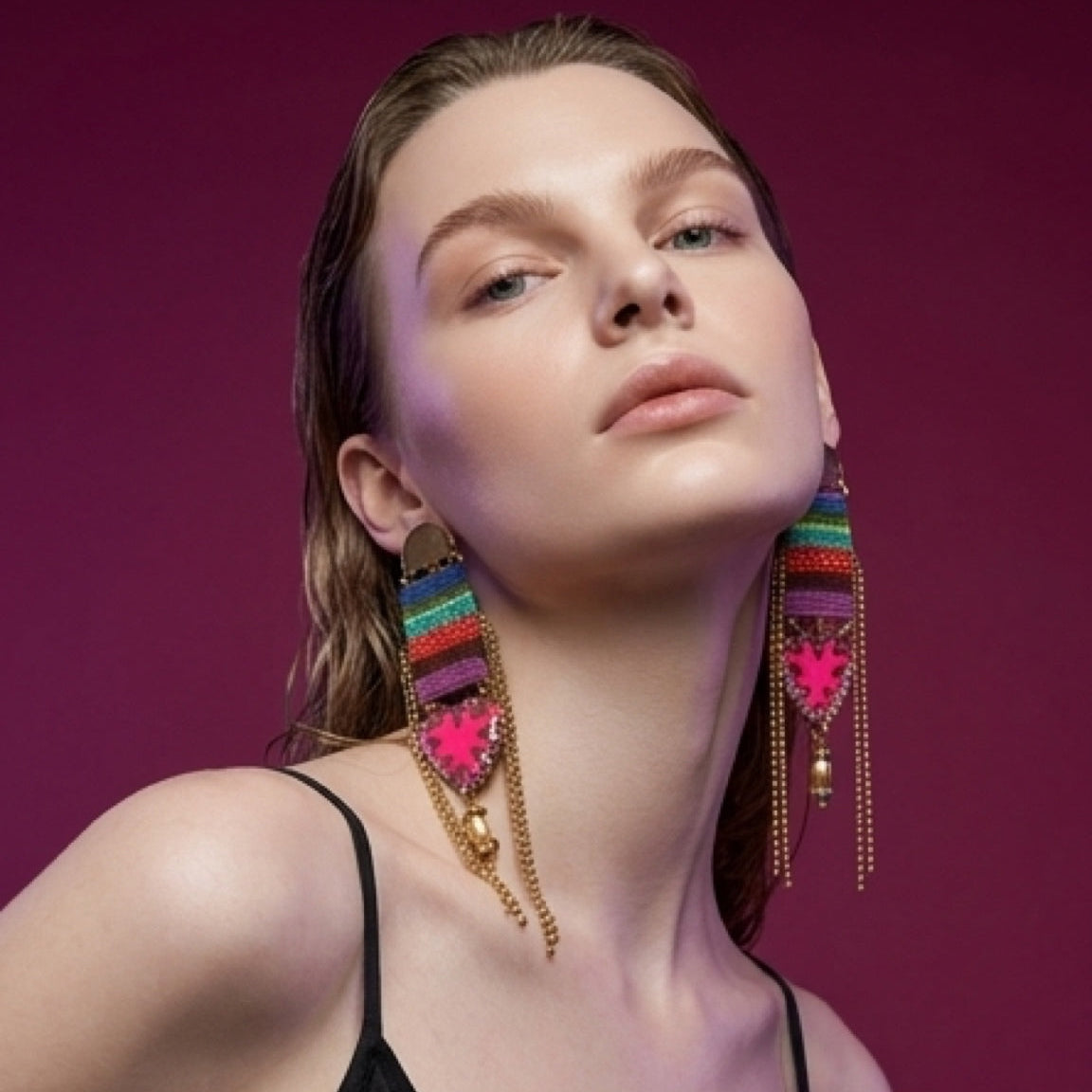 Woman wearing colorful earrings against a magenta background