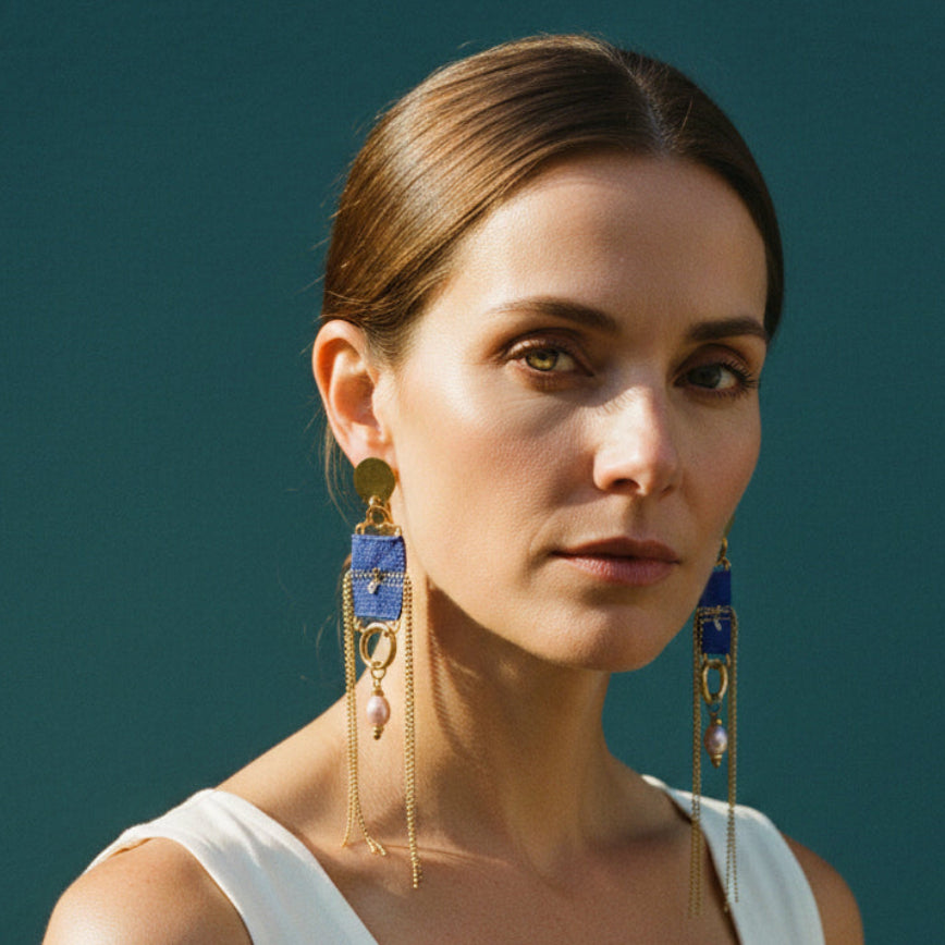 Pair of earrings with blue accents and chains on a light fabric background