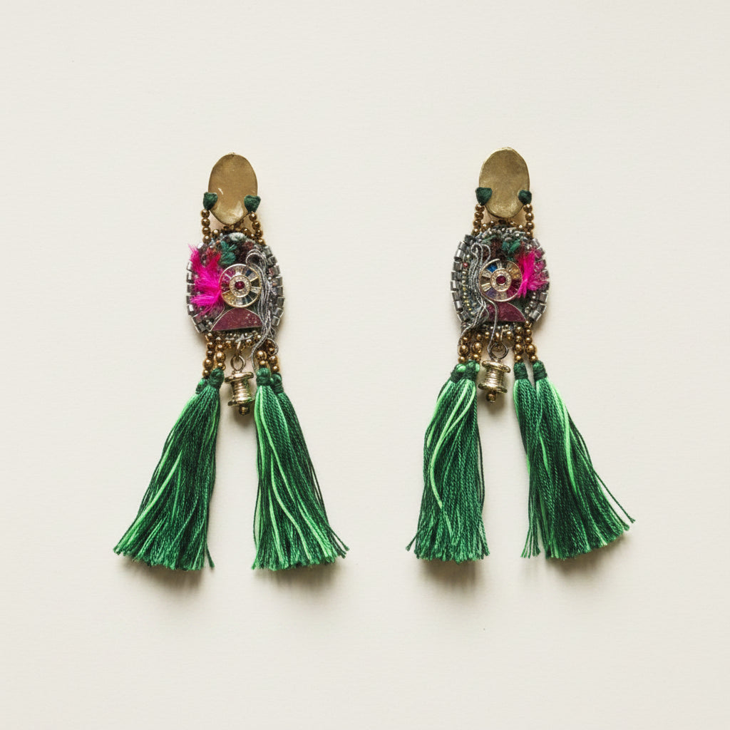 Pair of ornate earrings with green tassels on a light background