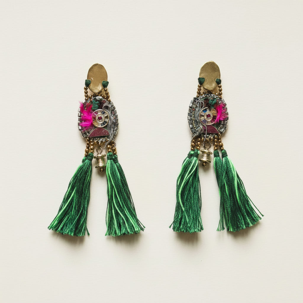 Pair of ornate earrings with green tassels on a light background
