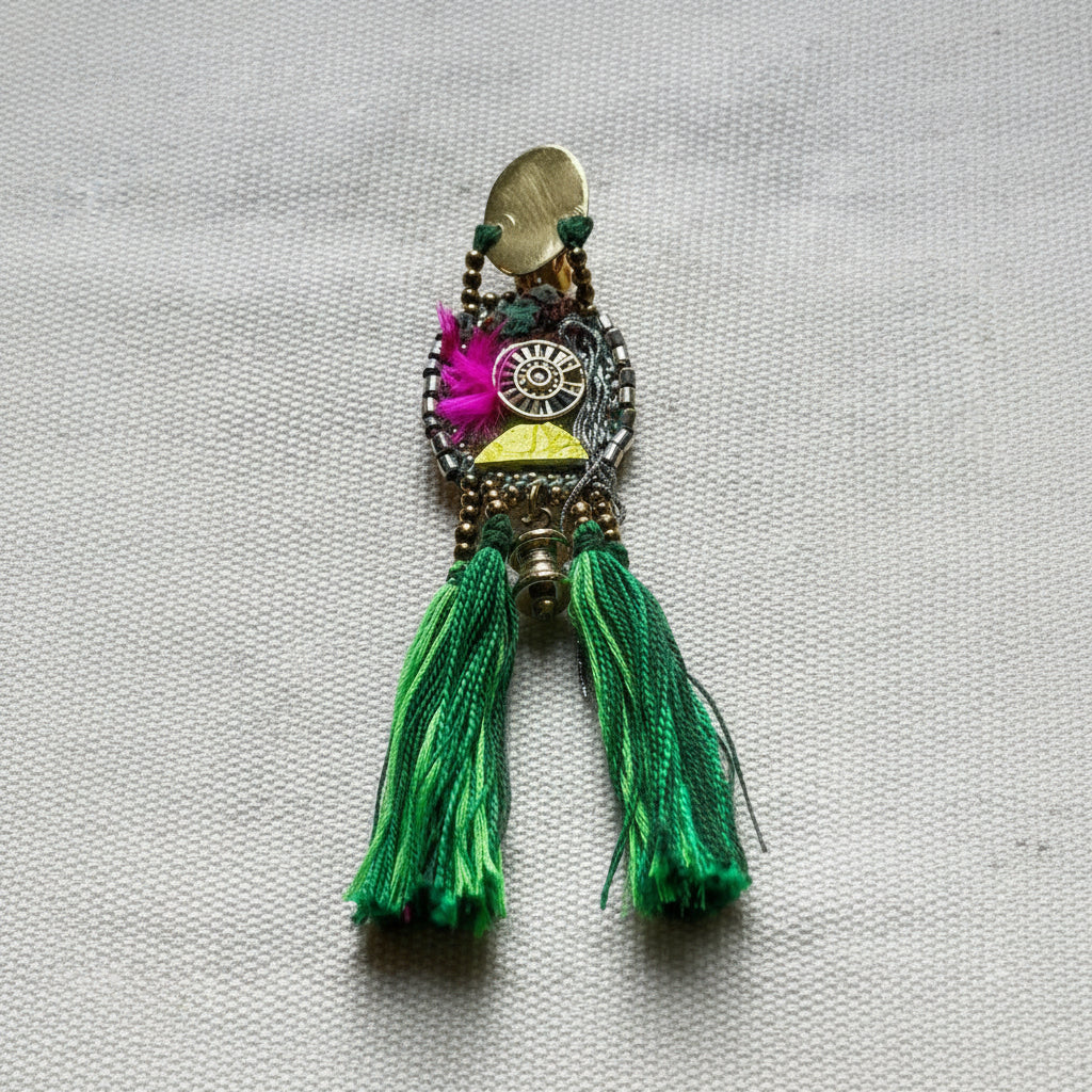 Decorative brooch with green tassels on a textured fabric background