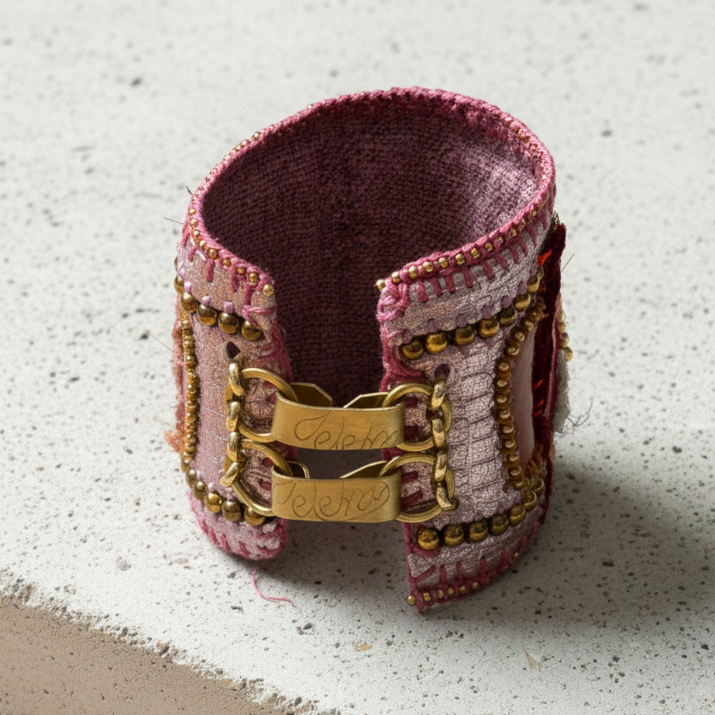 A handmade cuff bracelet made from dusty pink and purple textured fabric, decorated with gold-tone beads, chains, and a central gold clasp engraved with the names 'Celine' and 'Mery'.