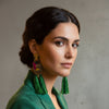 Woman wearing green tassel earrings in a blurred indoor setting
