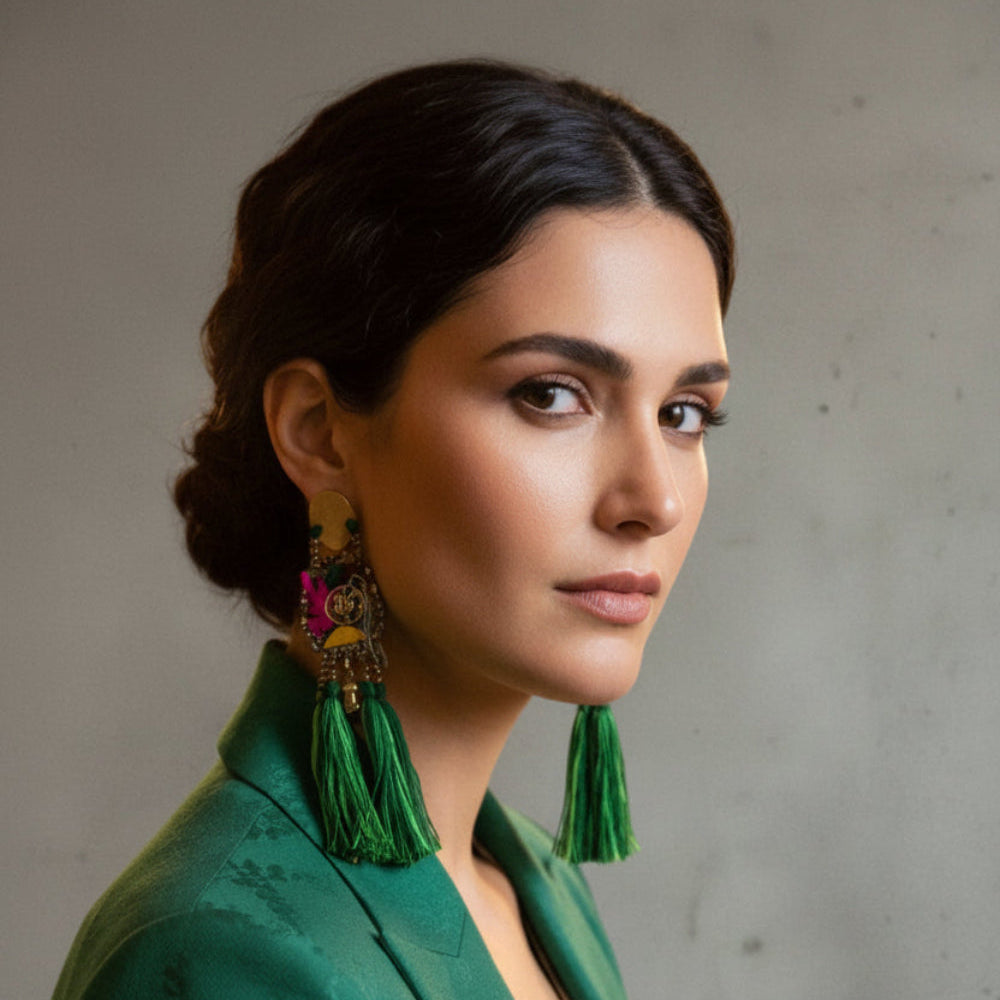 Woman wearing green tassel earrings in a blurred indoor setting