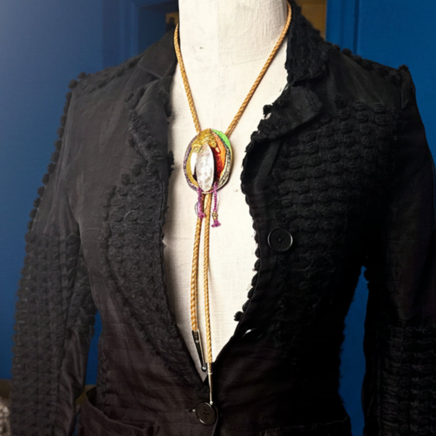 Black textured jacket on a mannequin with a colorful necklace against a neutral background