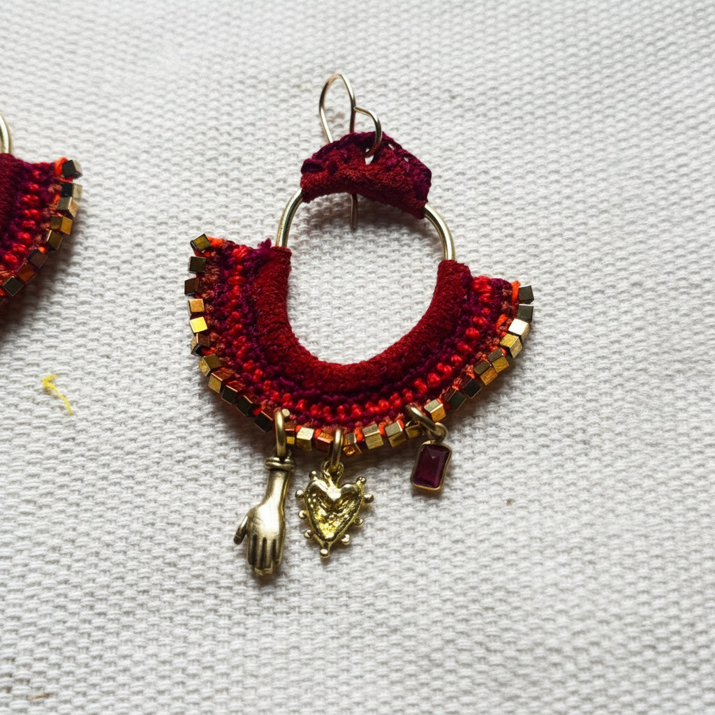 Red and gold macrame earrings with charms on a white fabric background