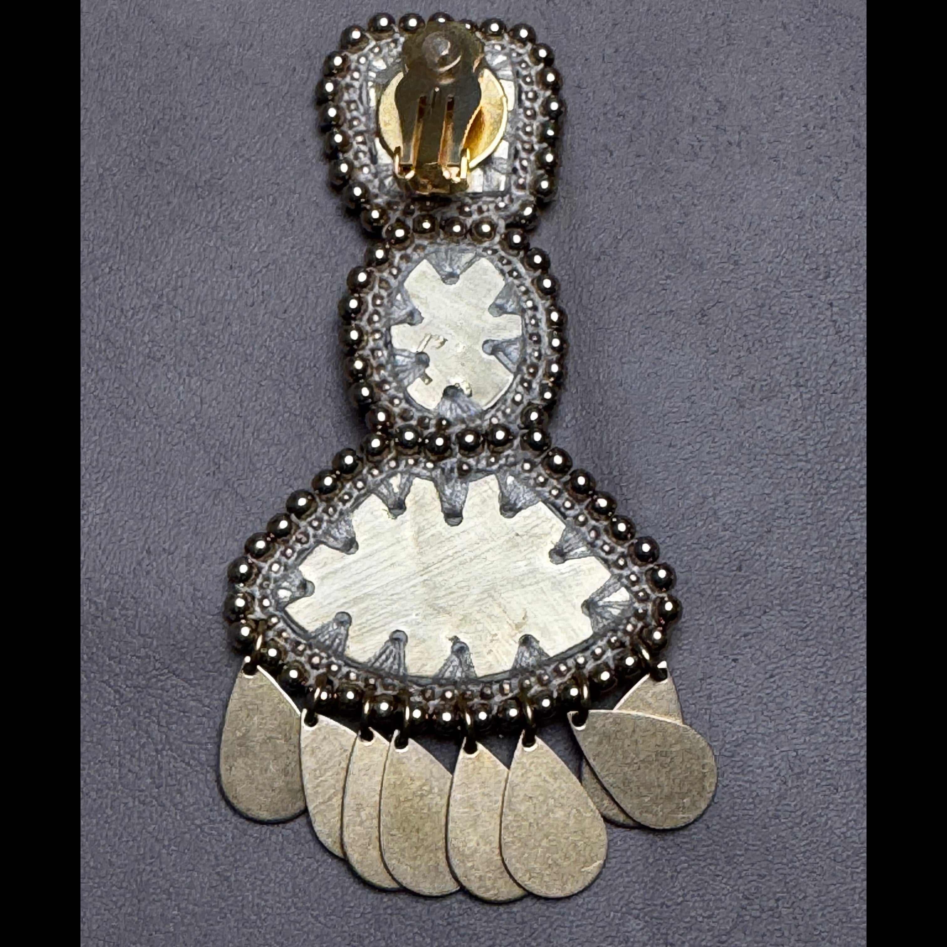 Decorative silver earring with intricate design on a gray background
