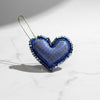 Heart-shaped blue and silver decorative item on a textured gray background