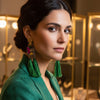 Woman wearing green tassel earrings in a blurred indoor setting