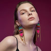 Woman wearing colorful earrings against a magenta background