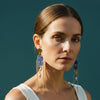 Pair of earrings with blue accents and chains on a light fabric background