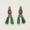 Pair of ornate earrings with green tassels on a light background
