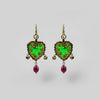 Pair of earrings with green and purple stones on a gray fabric background