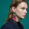 Woman wearing colorful earrings against a teal background
