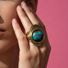 Gold ring with a blue stone on a hand with purple nail polish.