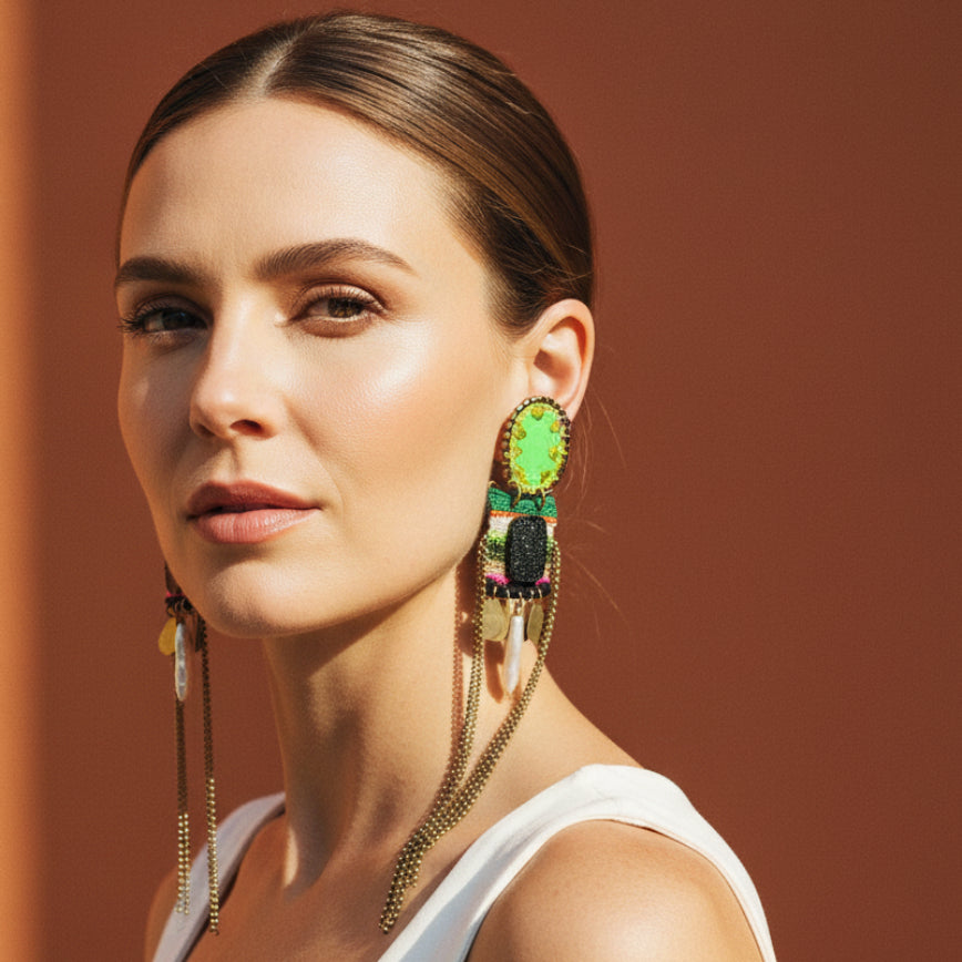 Pair of decorative earrings with green gemstones and chain designs on a light gray background
