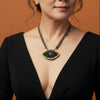 Woman wearing a black dress with a deep neckline and an eye-shaped pendant necklace.