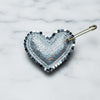 Heart-shaped brooch with metallic and iridescent design on a textured fabric background