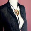 Mannequin wearing a black textured garment with a decorative bolo tie featuring a colorful pendant.