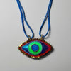 Colorful eye-shaped pendant on a blue cord against a textured beige background