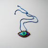 Colorful eye-shaped pendant on a blue cord against a textured white background