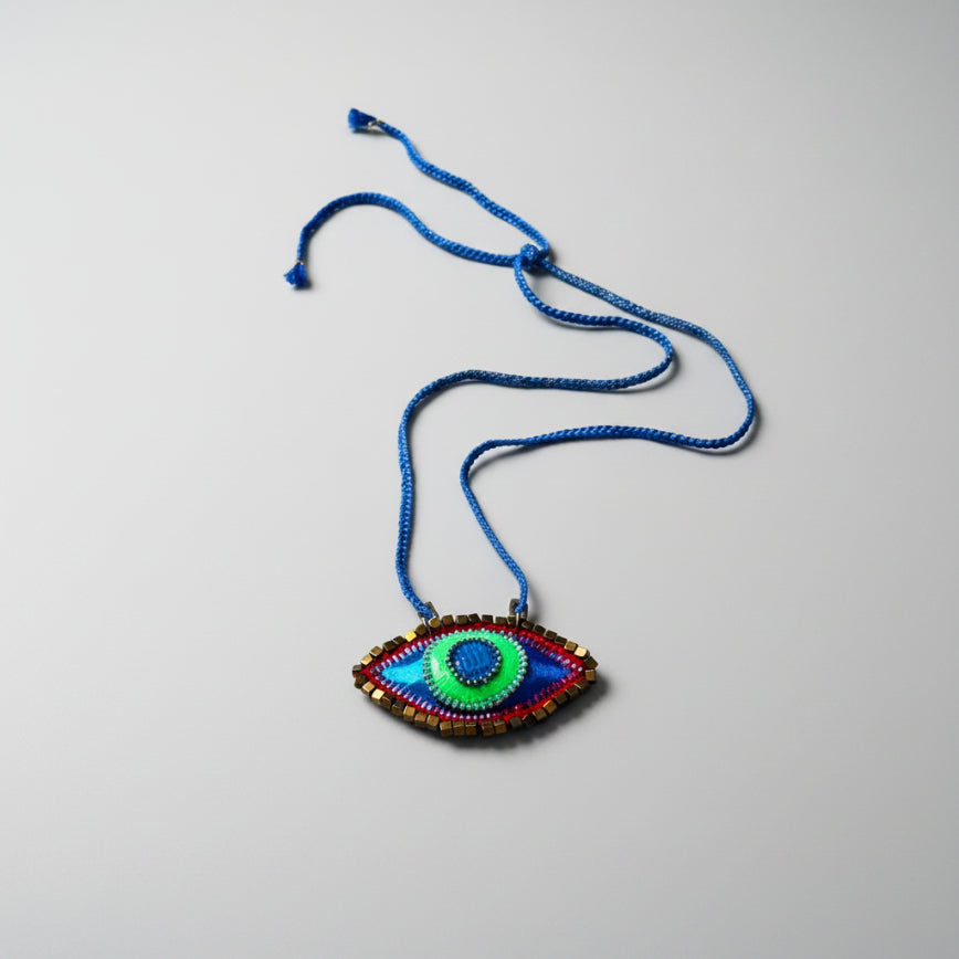 Colorful eye-shaped pendant on a blue cord against a textured white background